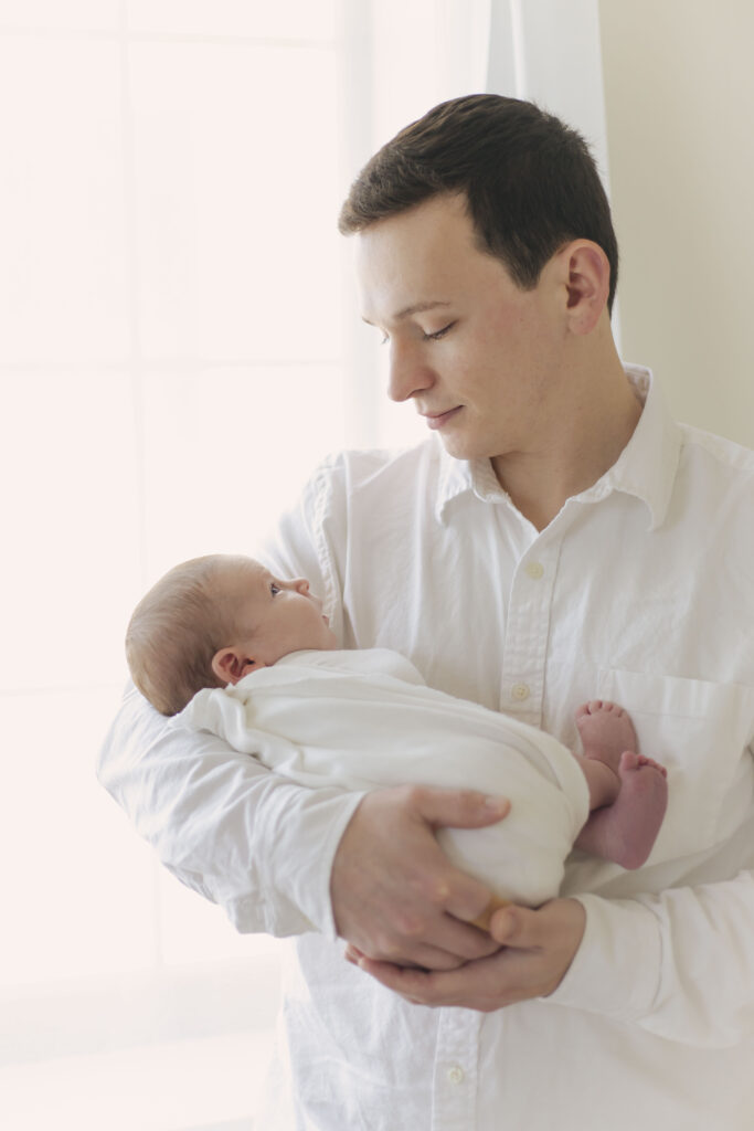 dad holding newborn baby posing for their  newborn session showcasing dad's outfit 