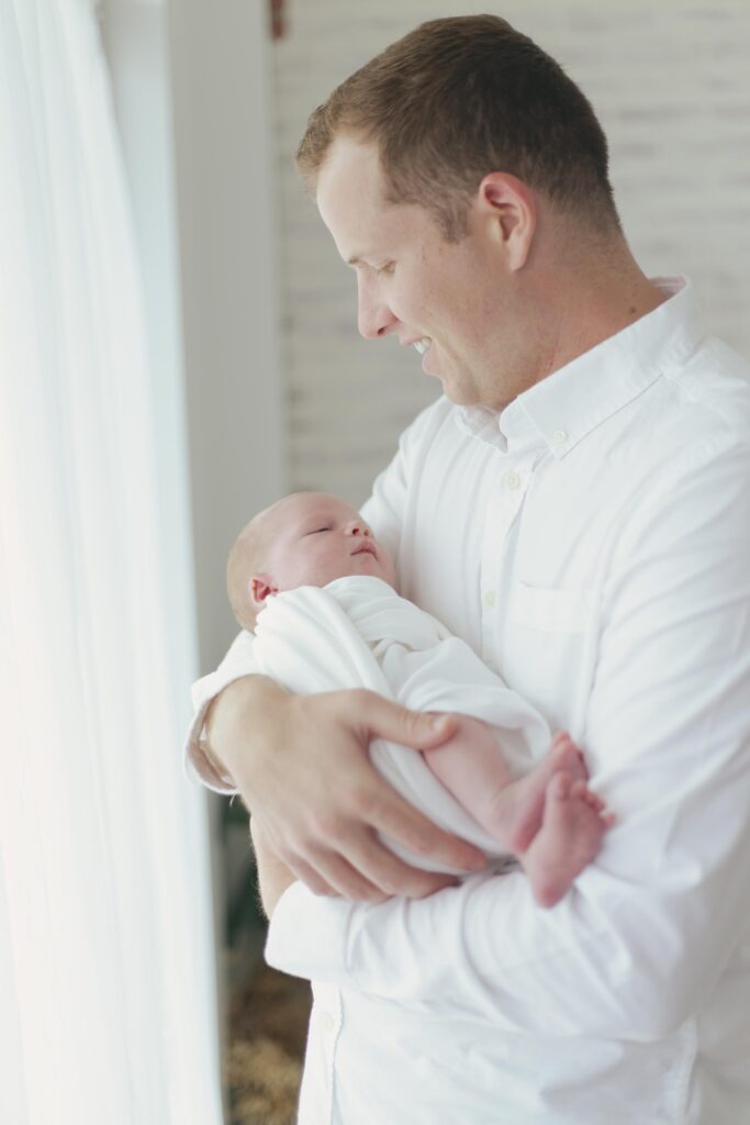 dad holding newborn baby posing for their  newborn session showcasing dad's outfit 