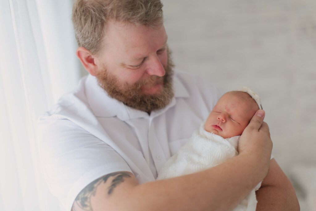 dad holding newborn baby posing for their newborn session showcasing dad's outfit