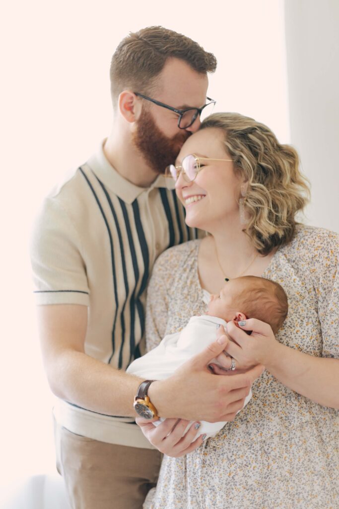 mom and dad posing with their newborn for their newborn photo showcasing dad's outfit 
