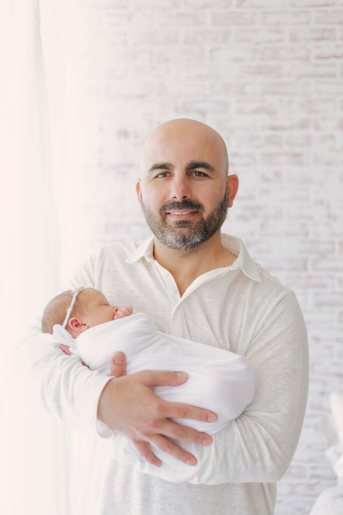 dad holding newborn baby posing for their  newborn session showcasing dad's outfit 