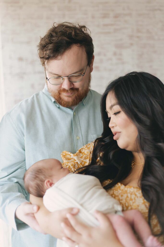 mom and dad posing with their newborn for their newborn photo showcasing dad's outfit 