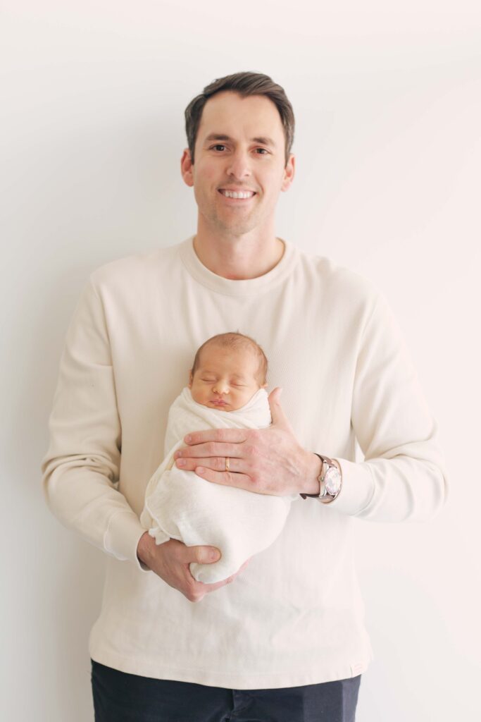 dad holding newborn baby posing for their  newborn session showcasing dad's outfit 