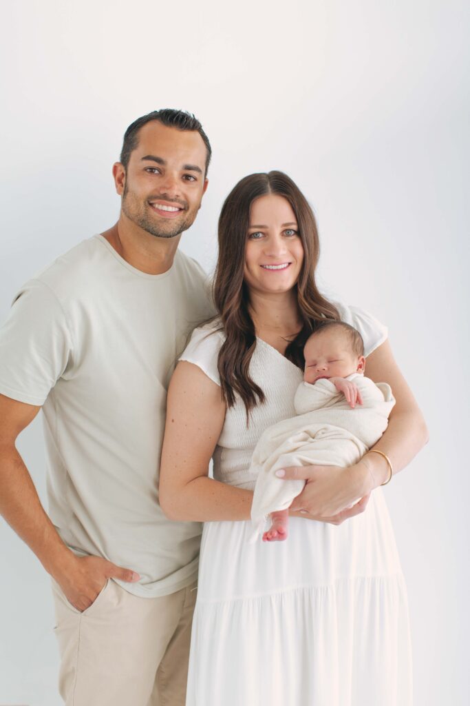 mom and dad posing with their newborn for their newborn photos showcasing dad's outfit 